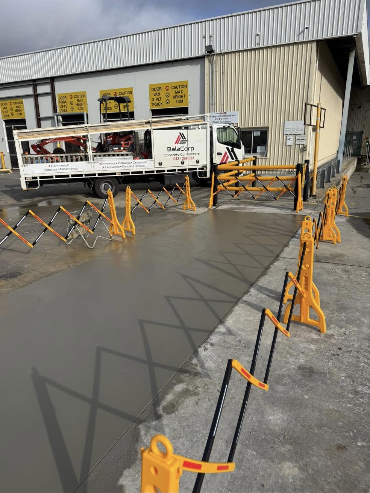 BalaCorp truck at a warehouse loading dock with a freshly poured concrete slab and safety barriers