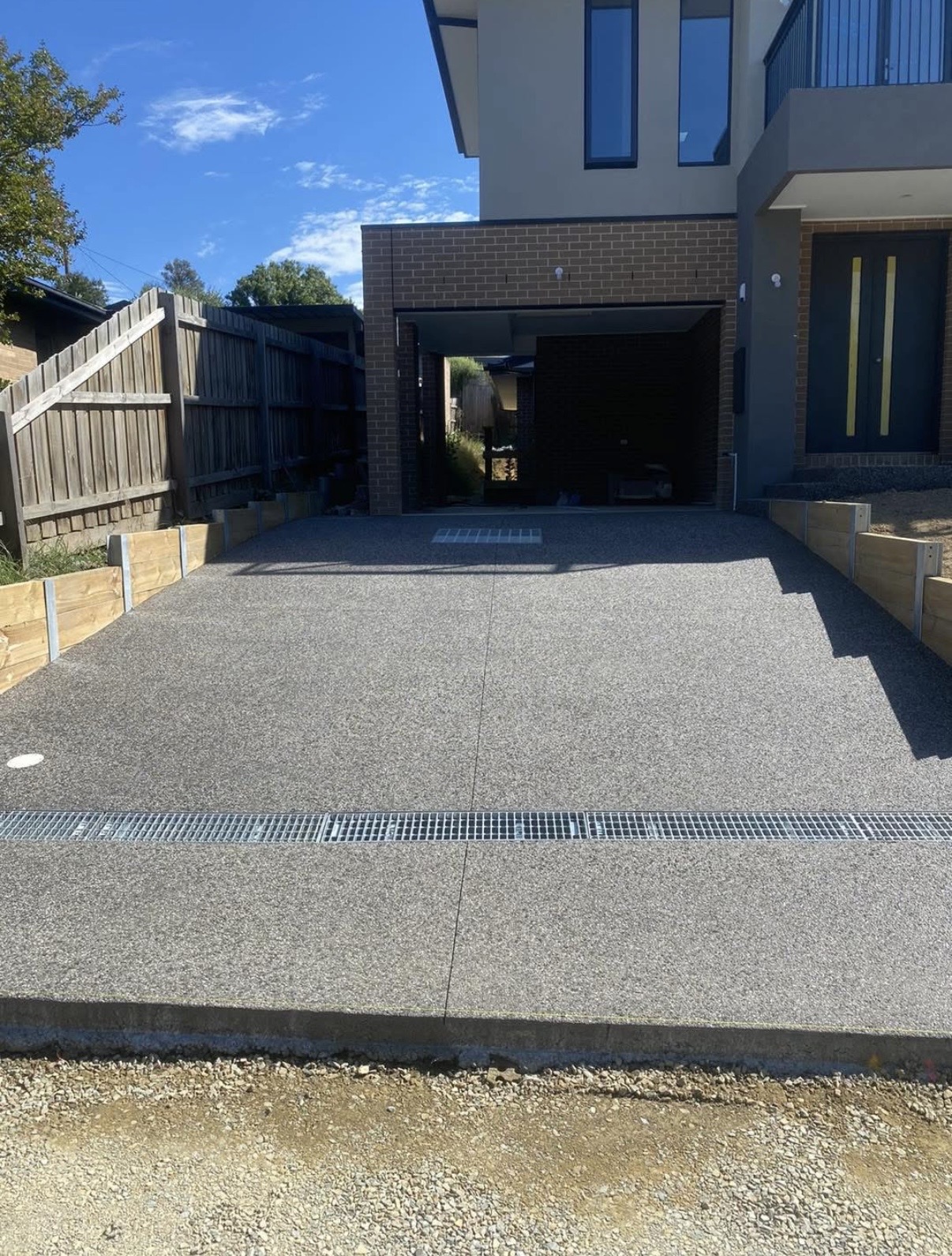 Exposed aggregate driveway with a grated channel drain across the crossover of a modern townhouse
