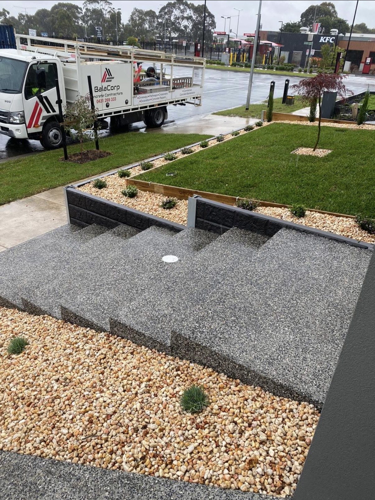 Exposed aggregate entry landing and steps with charcoal retaining walls and a BalaCorp truck on the street