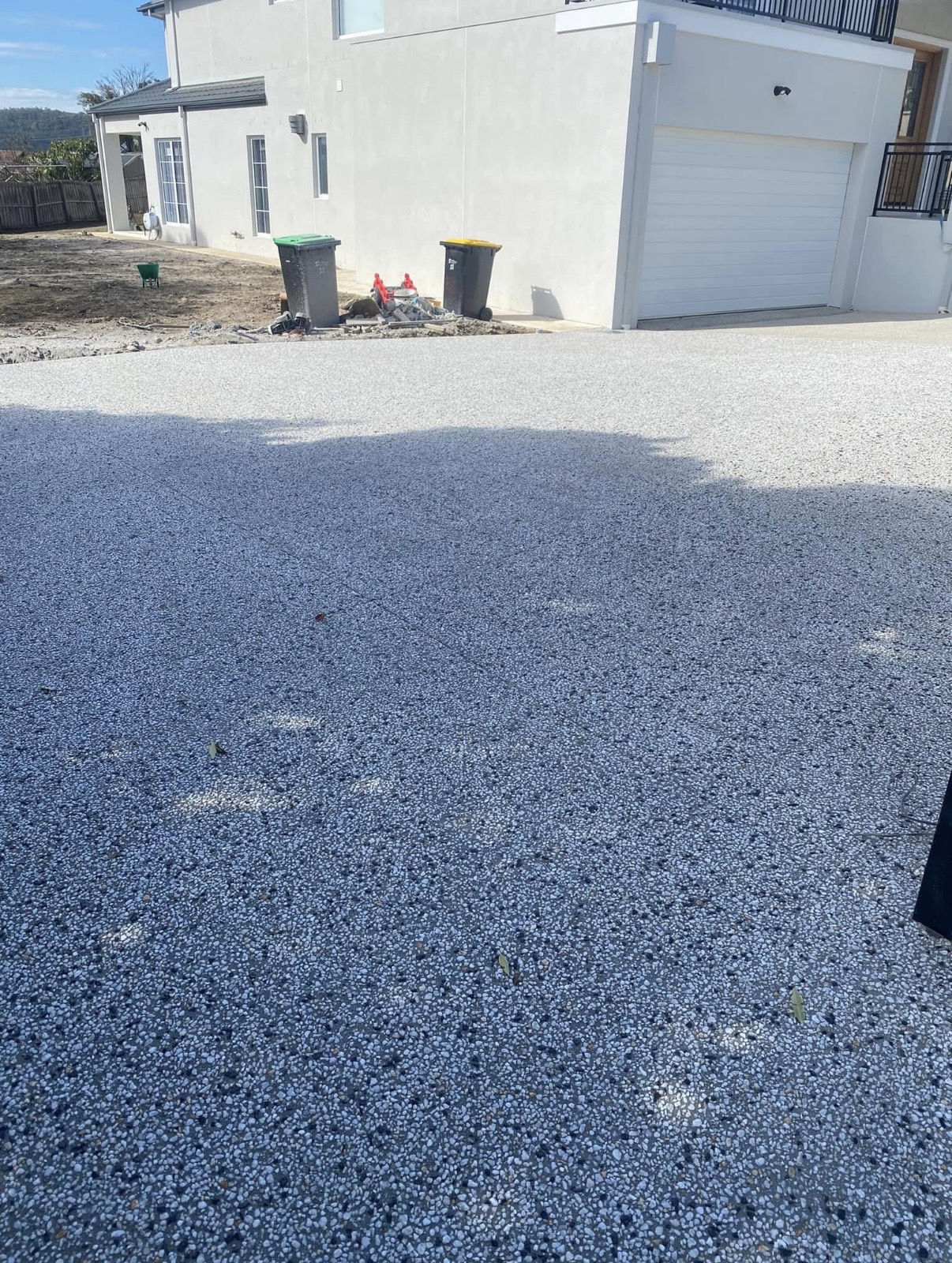 Large exposed aggregate driveway apron in front of a rendered two-storey home with a double garage