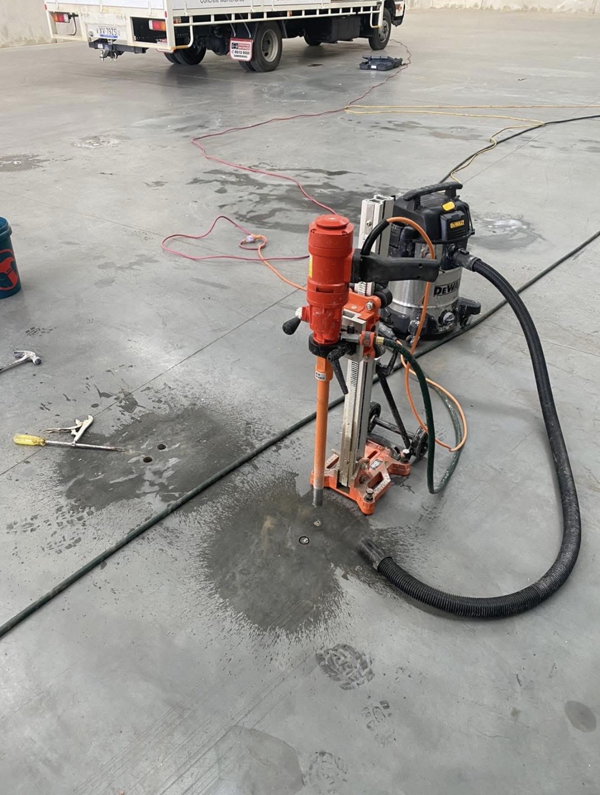 Core drill rig cutting into a finished concrete warehouse slab with a work truck in the background